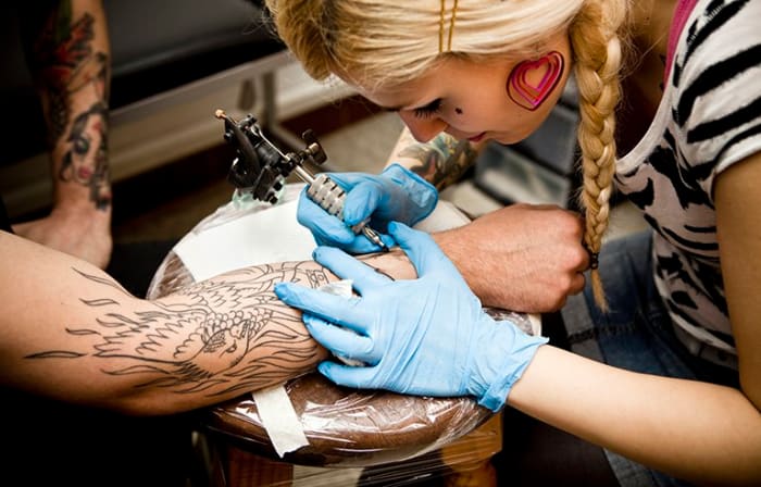 Közelkép egy fiatal nőről, aki tetoválást készít a fiatalember karjában.