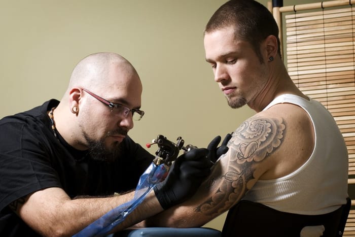 Tetováló, aki arra összpontosít, hogy valakinek tetoválást adjon egy fiatalembernek