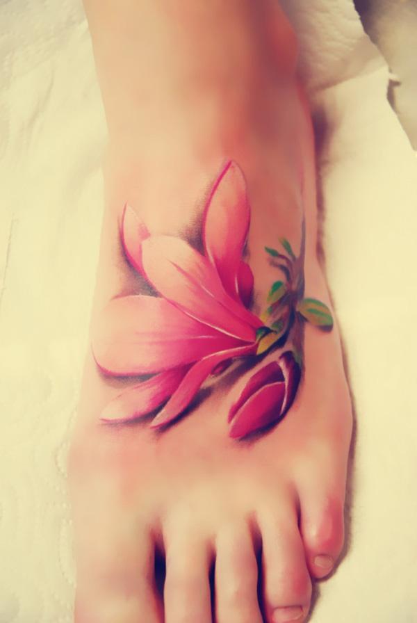 Den realistiske magnolia -tatoveringen ser ut som et stykke blomst faller på foten