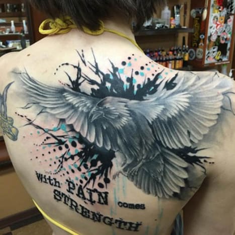 Ravn og sitat tilbake -tatovering Denne kvinnens tatovering på ryggen ble blekket av Josh A. fra Clever Rebel Tattoo i staten Washington, og har et svart -hvitt bilde av en ravn på flukt med sitatet 