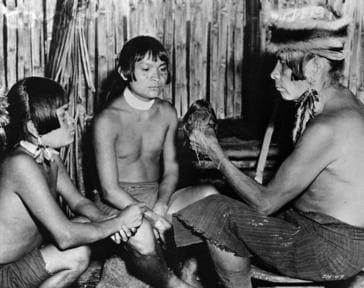 15. februar 1953, Ecuador --- Original bildetekst: En medisinmann som holder et krympet hode, instruerer to ungdommer i plikten til medlemmer av Jivaro-stammen. De dreper
