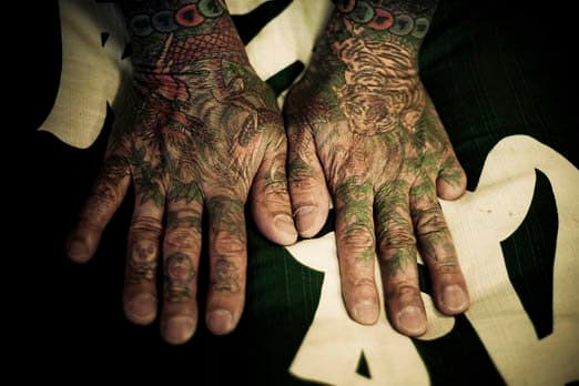 Tetovált kezek, számjegy hiányzik. A hagyományos japán tetoválás, amelyet a Yakuza gyakran használ, egy nagyon régi és időigényes folyamat, amikor manuálisan felragasztunk egy botot a bőr több éles tűvel. Ennek pontos szögben (a bőr vastagságától függően) és pontos sebességgel (120/perc) kell megtörténnie, és ez a készség csak a hagyományos japán tetováló mesterekre jellemző. Az eredmény egy bonyolultság, egy színpaletta és egy minta, amely nem lehetséges a géppel végzett tetoválás modern módjával. Hori Sensei tetováló mester meghívja Önt, nem fogad rendszeres ügyfeleket. Nála a hagyományos japán tetoválás elkészítése körülbelül 100 órát vesz igénybe, akár 10 000 dollárba is kerülhet, és napi vagy heti látogatások ütemezését kell elkészíteni. Ügyfélként csak egy kis beleszólása van a tetoválás kialakításába. Hori Sensei határozza meg, hogy mi a legjobb az Ön számára, miután időt szakított arra, hogy beszéljen veled és megismerje. Csak néhány hagyományos japán tetováló szakértő él ma is Japánban. - 2009