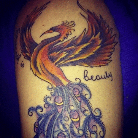 Her er hennes Phoenix/Peacock -tatovering på øvre venstre arm. Hun kombinerte dem for å vise sin styrke og eleganse til verden og seg selv. Ved siden av fuglen står det: