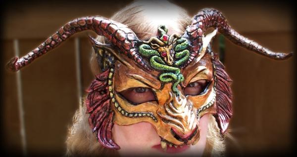 CHIMERA MASK En maske basert på det mytiske monsteret, Chimera, i rikt gull, oransje og rødt. Tradisjonelt hadde kimæren en løvekropp, en løve og geitehoder og en ormhale. Kunstneren ga masken hodet til en hornet løve med en slange som sno seg ned i trynet og geitemblemet på pannen. Geiten og slangen har skinnende røde øyne, og en rød dråpe ligger i slangeens panne. Masken er helt håndskulpturert og malt som har et kunstnerstempel på baksiden med datoen den ble opprettet. Masken er lett og hornene er noe fleksible for å redusere risikoen for skade. Med horn er merket 14